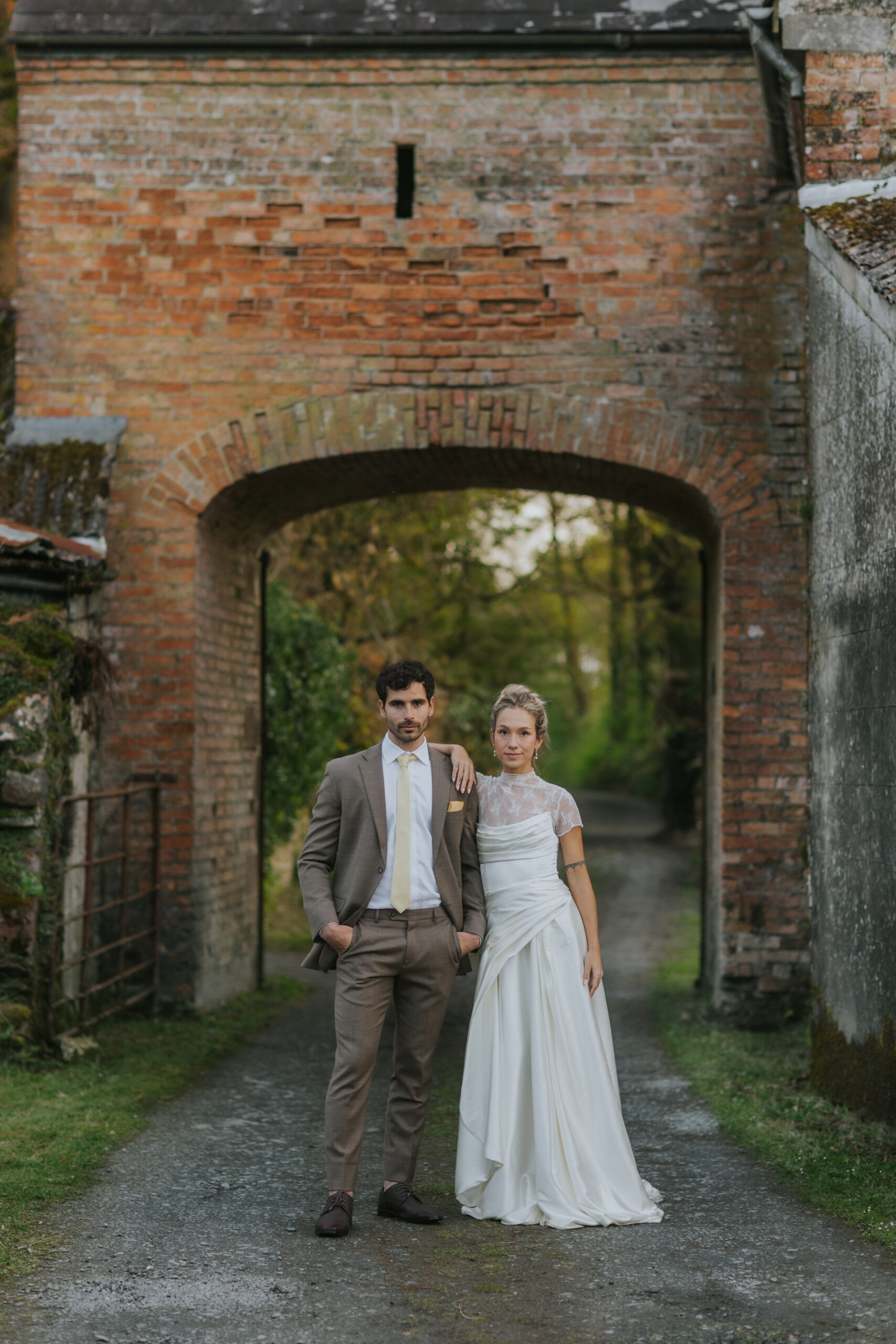Bride and groom posing beneath an old brick arch.