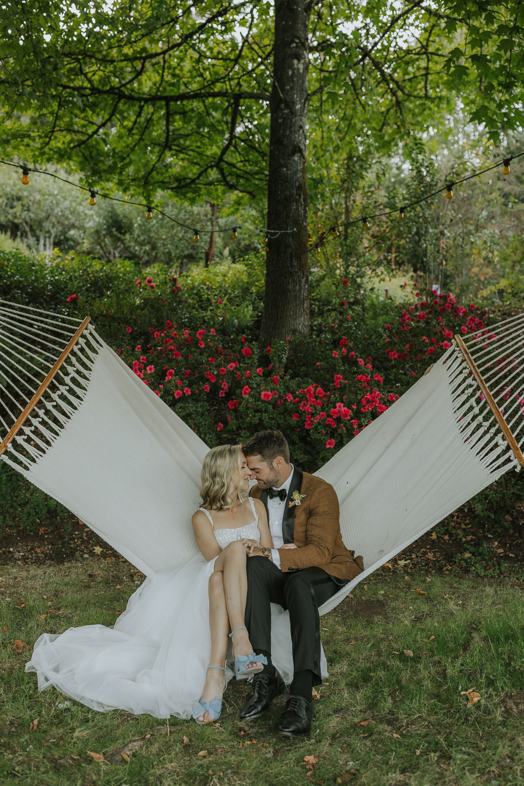 Bride and groom relaxing together in a hammock surrounded by blooming roses.