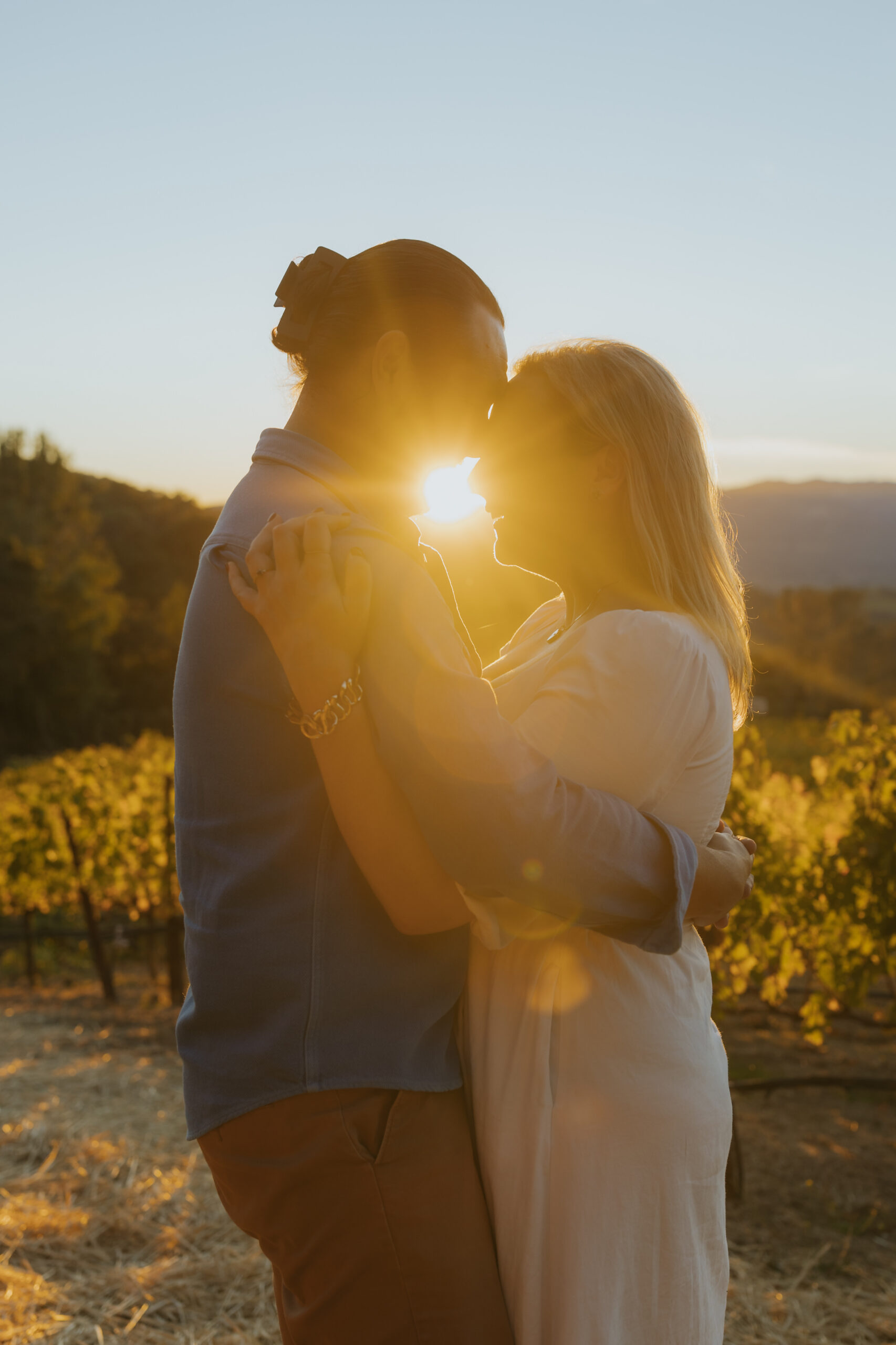 Georgia and Tim kissing in glowing sunset light during their Napa Valley winery engagement session.