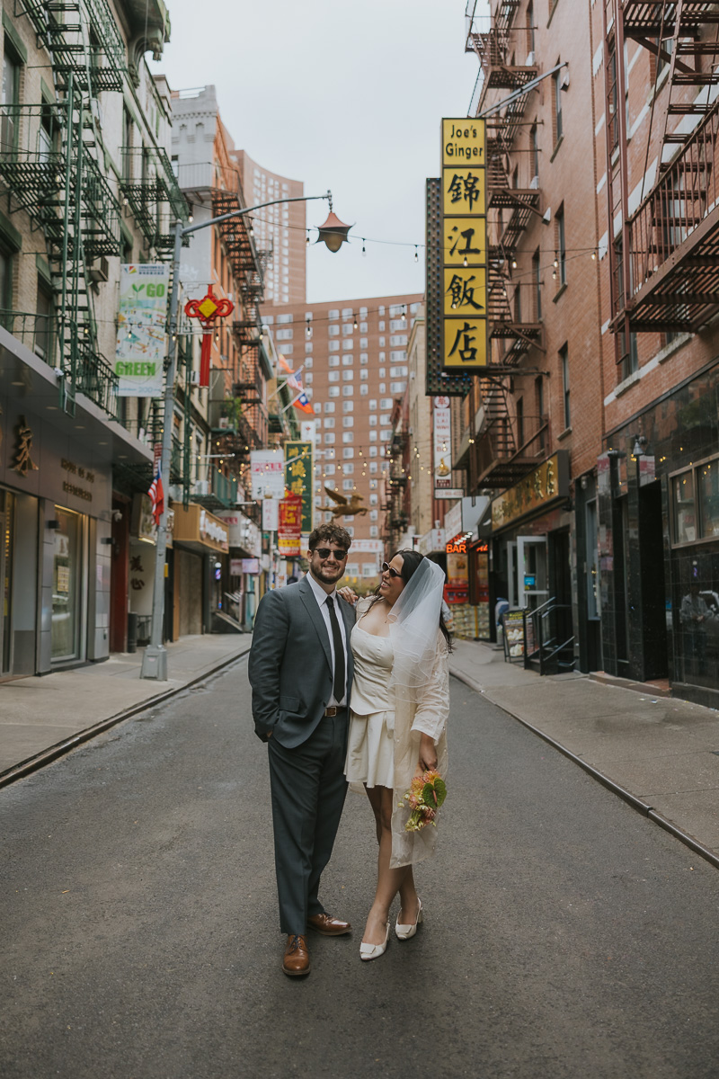 Megan and Dylan stand together in the middle of a colorful Chinatown street after their wedding.